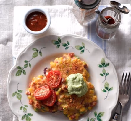 A plate of sweetcorn and chorizo fritters topped with tomatoes and avocado