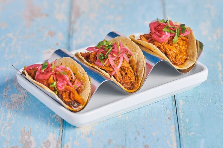 Three smaller pork pibil filled tacos, topped with pink pickled onion