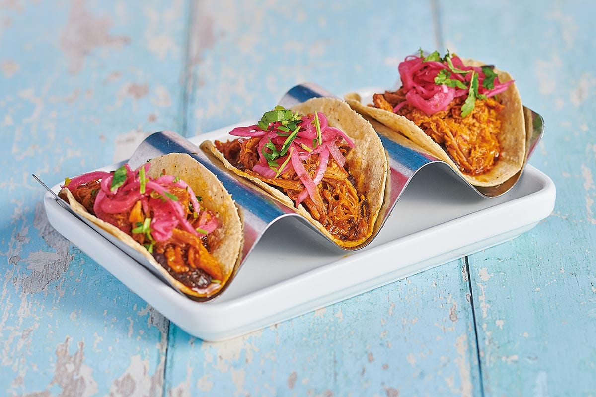 Three smaller pork pibil filled tacos, topped with pink pickled onion