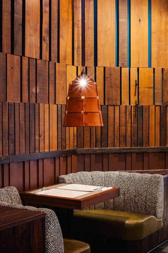 Intimate and cosy seating at Wahaca wimbledon. A table for two is flanked by two cosy armchairs with a single low hanging light hanging over the table. The walls are made of wooden panels.