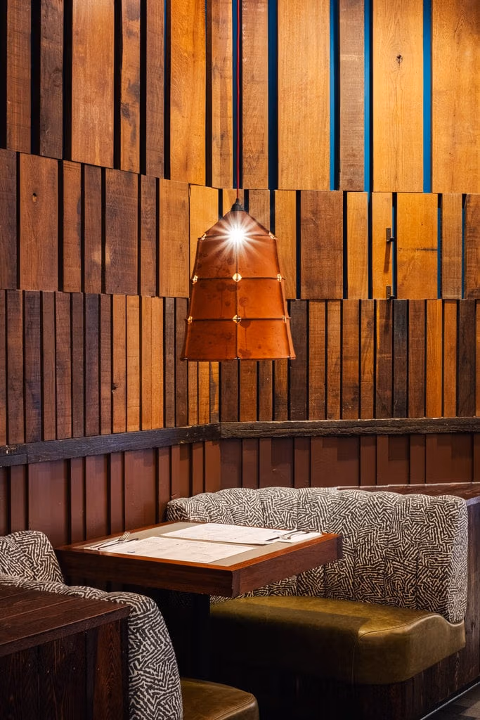 Intimate and cosy seating at Wahaca wimbledon. A table for two is flanked by two cosy armchairs with a single low hanging light hanging over the table. The walls are made of wooden panels.