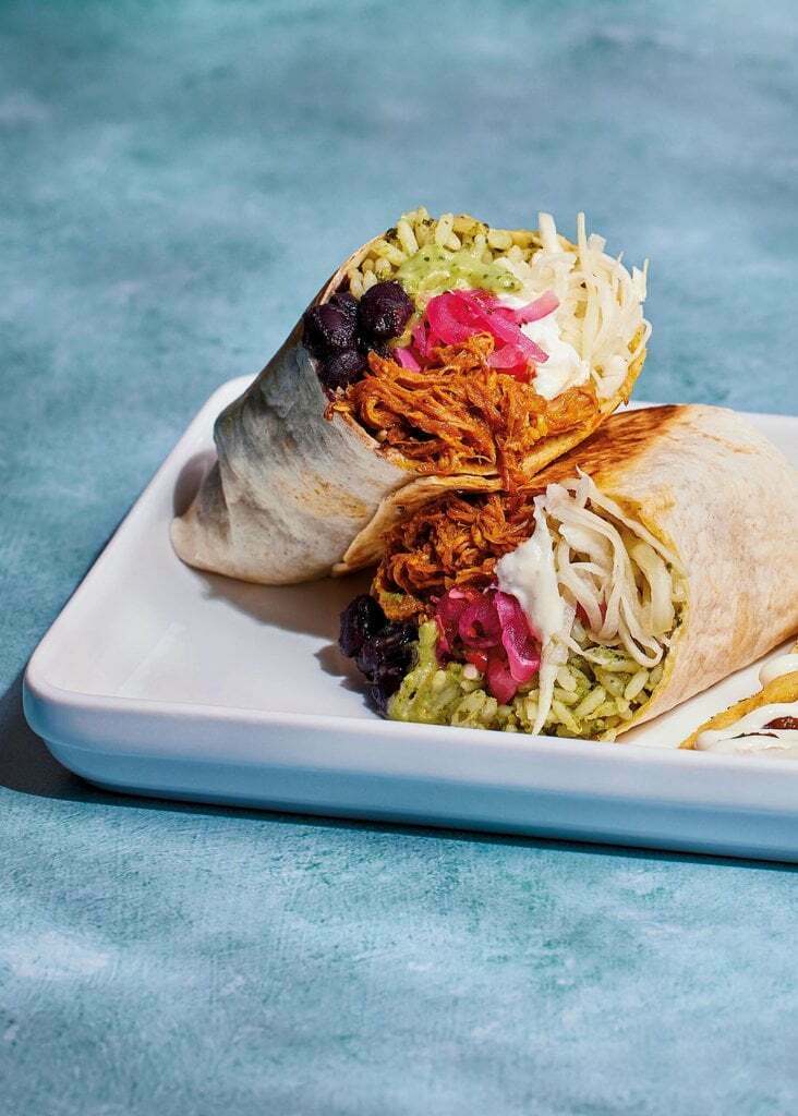 Pork burrito cut in half to reveal the delicious ingredients packed inside - pork pibil, black beans, rice, slaw, crema and pink pickled onions