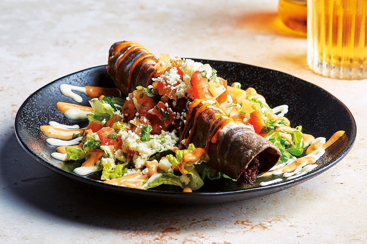 Vibrant sweet potato and feta taquito topped with fresh tomatoes, lettuce and feta