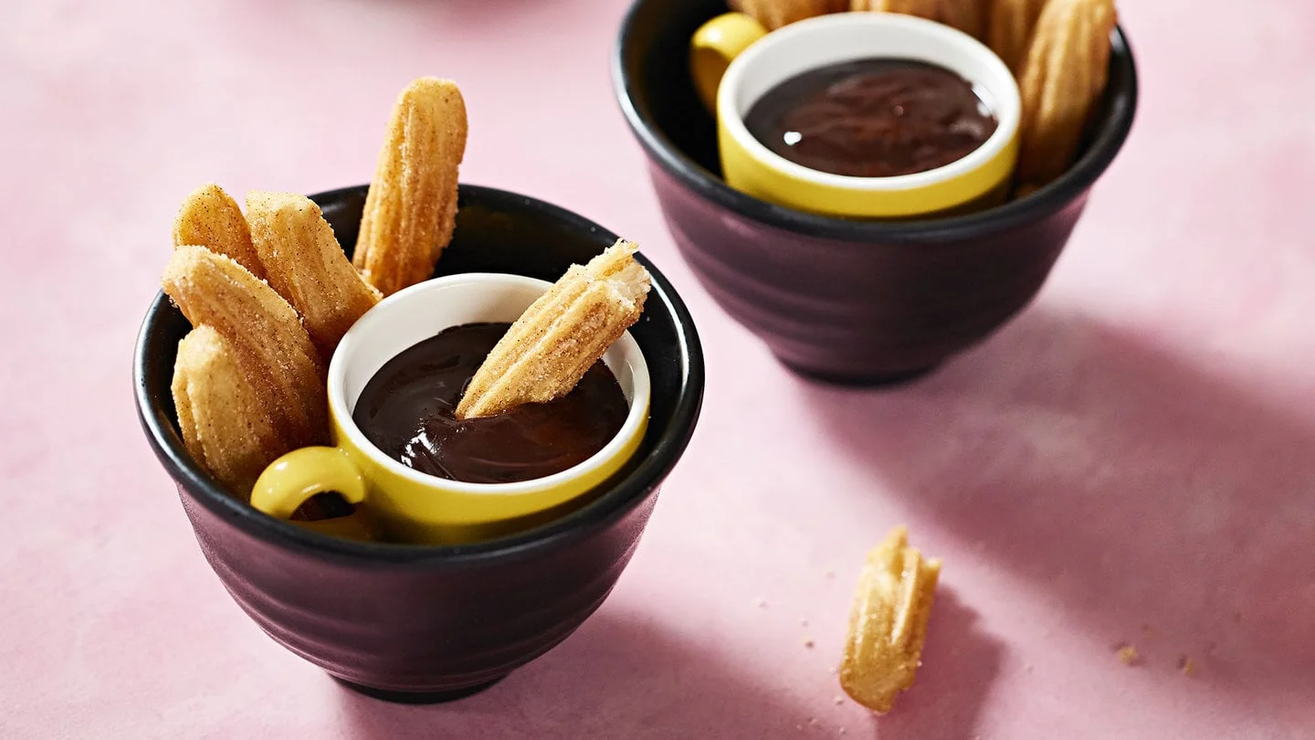 A bowl of churros served with a cup of warm chocolate sauce
