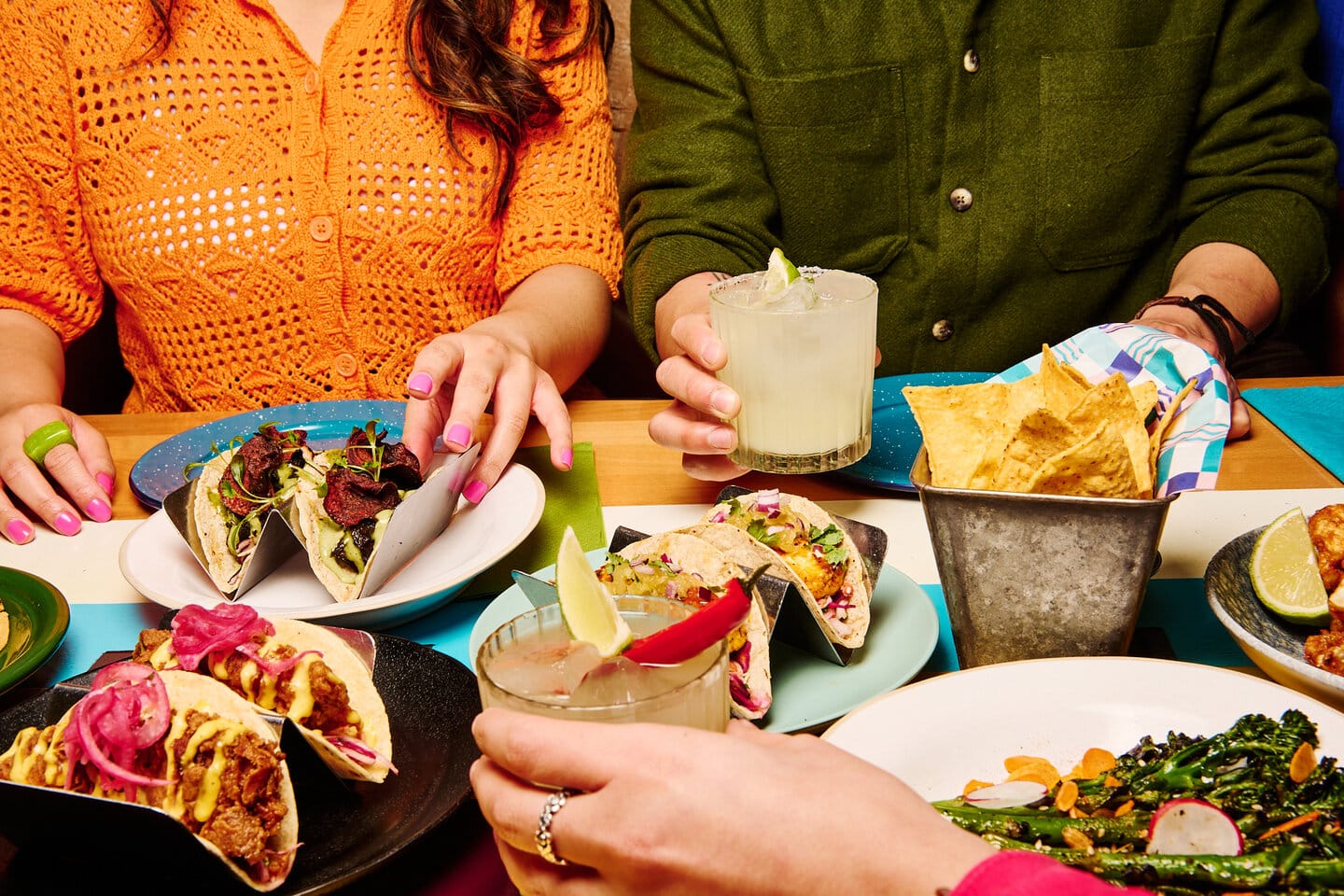 A group of people around a Wahaca table tucking into tacos and sides, with margaritas