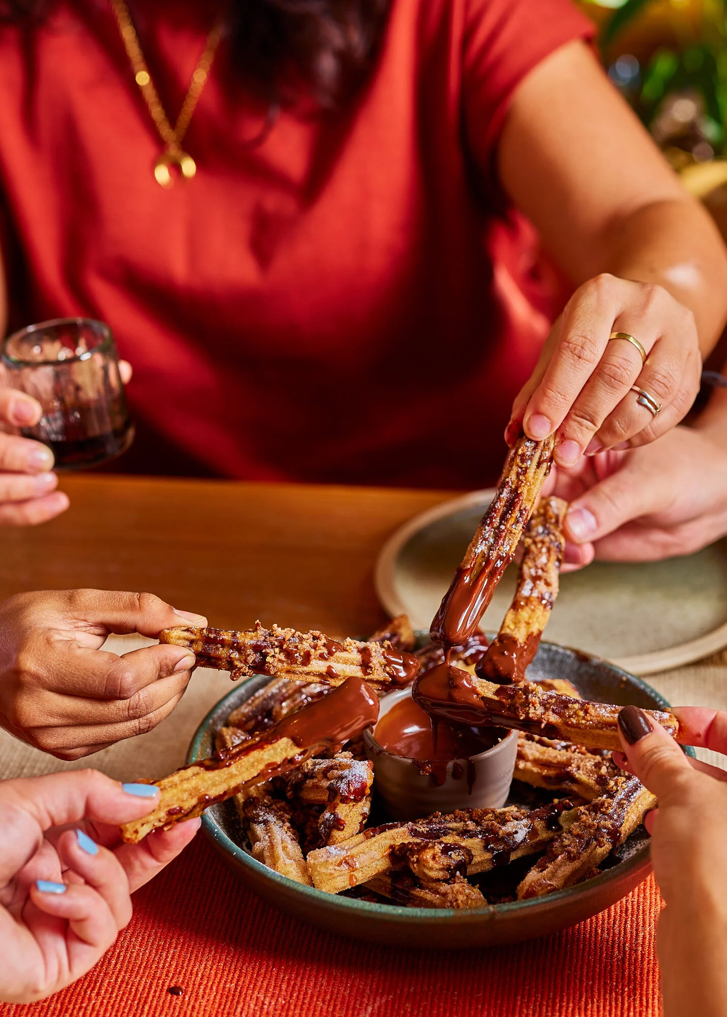 Many hands dipping churros into warm chocolate sauce