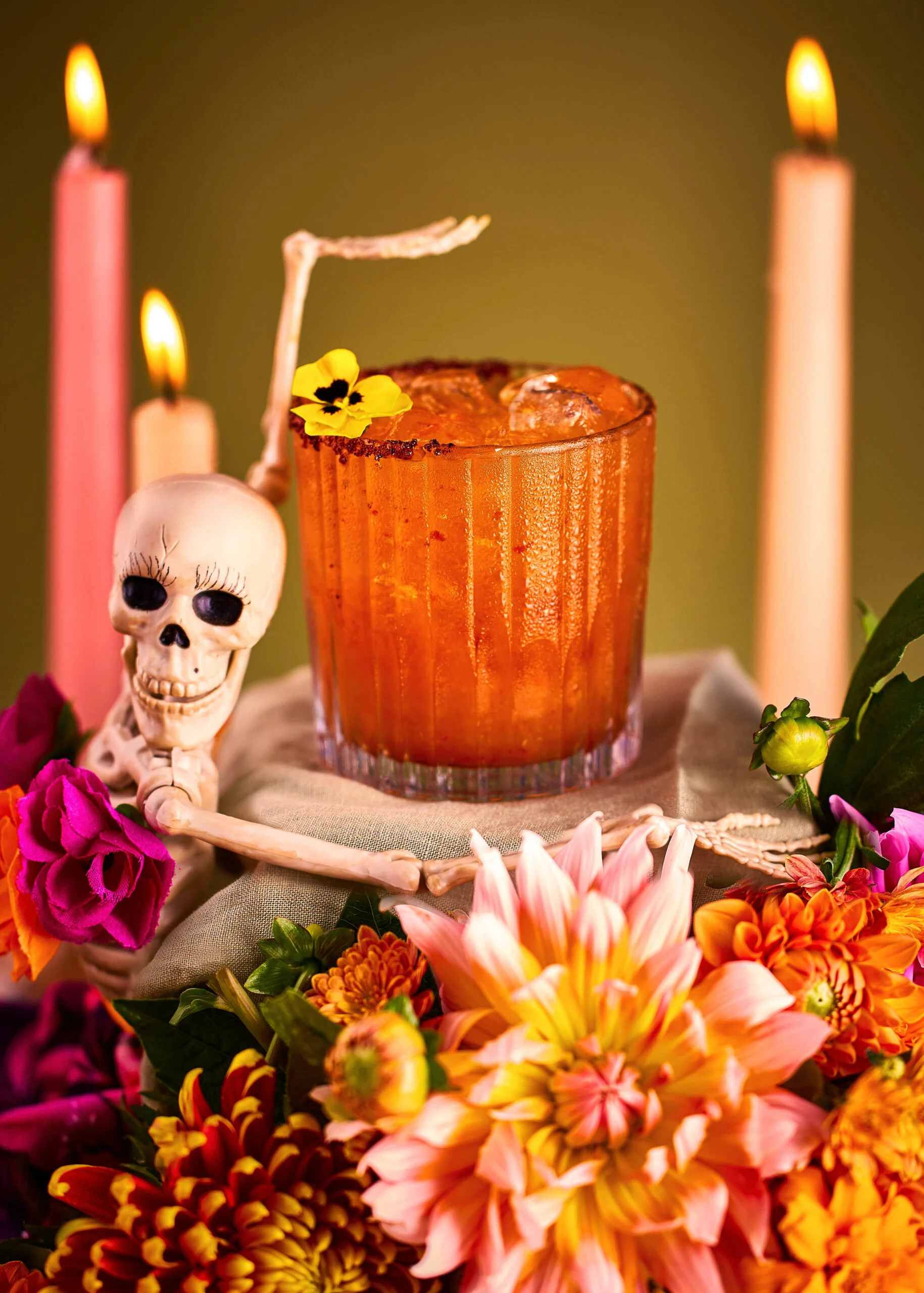 Day of the dead Mezcalita cocktail with flowers, candles and a Mexican calaca surrounding the drink