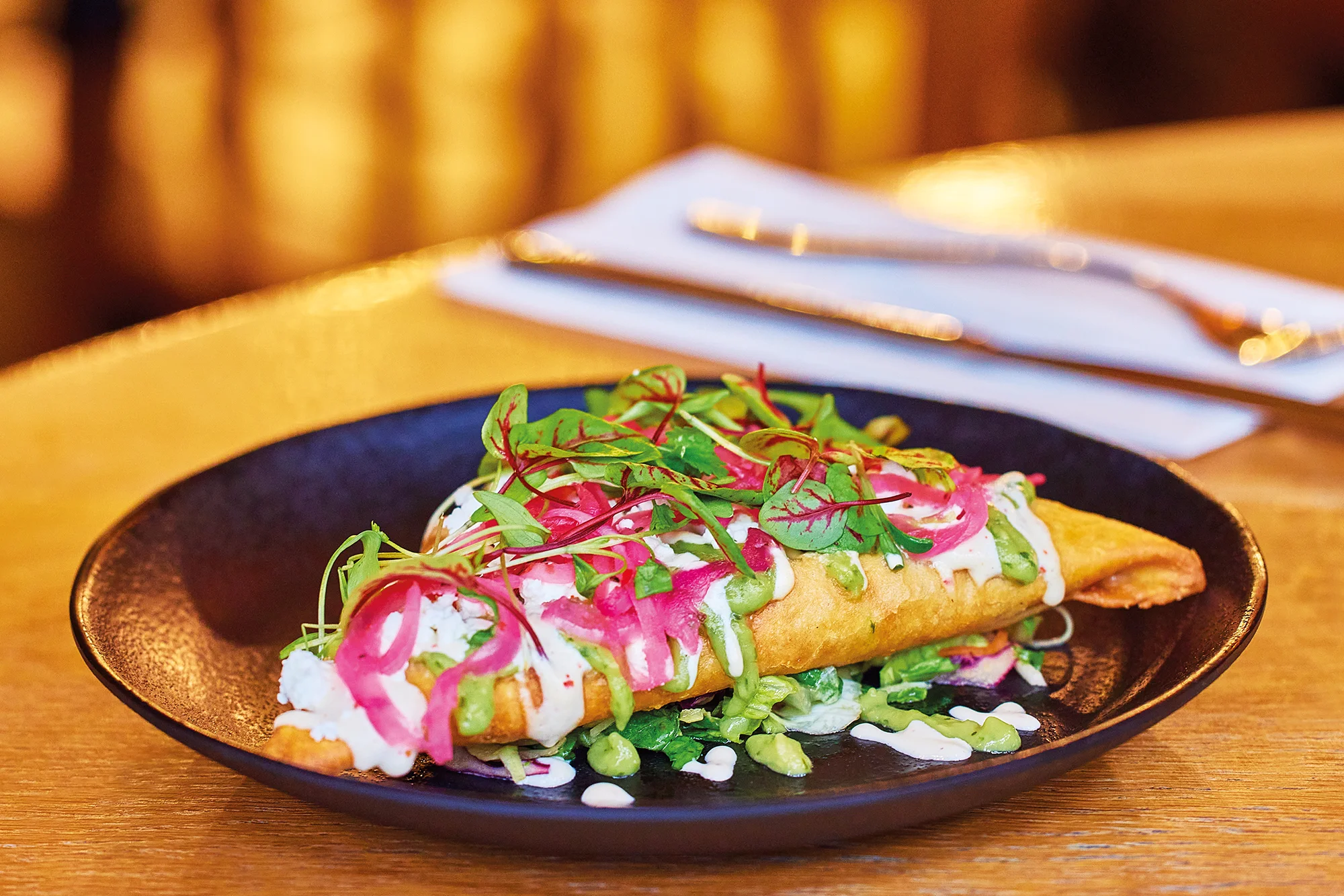 Our tetela special - a tortilla parcel packed with veggies and black beans, topped with vibrant pink pickled onions, avocado crema and a cashew crema