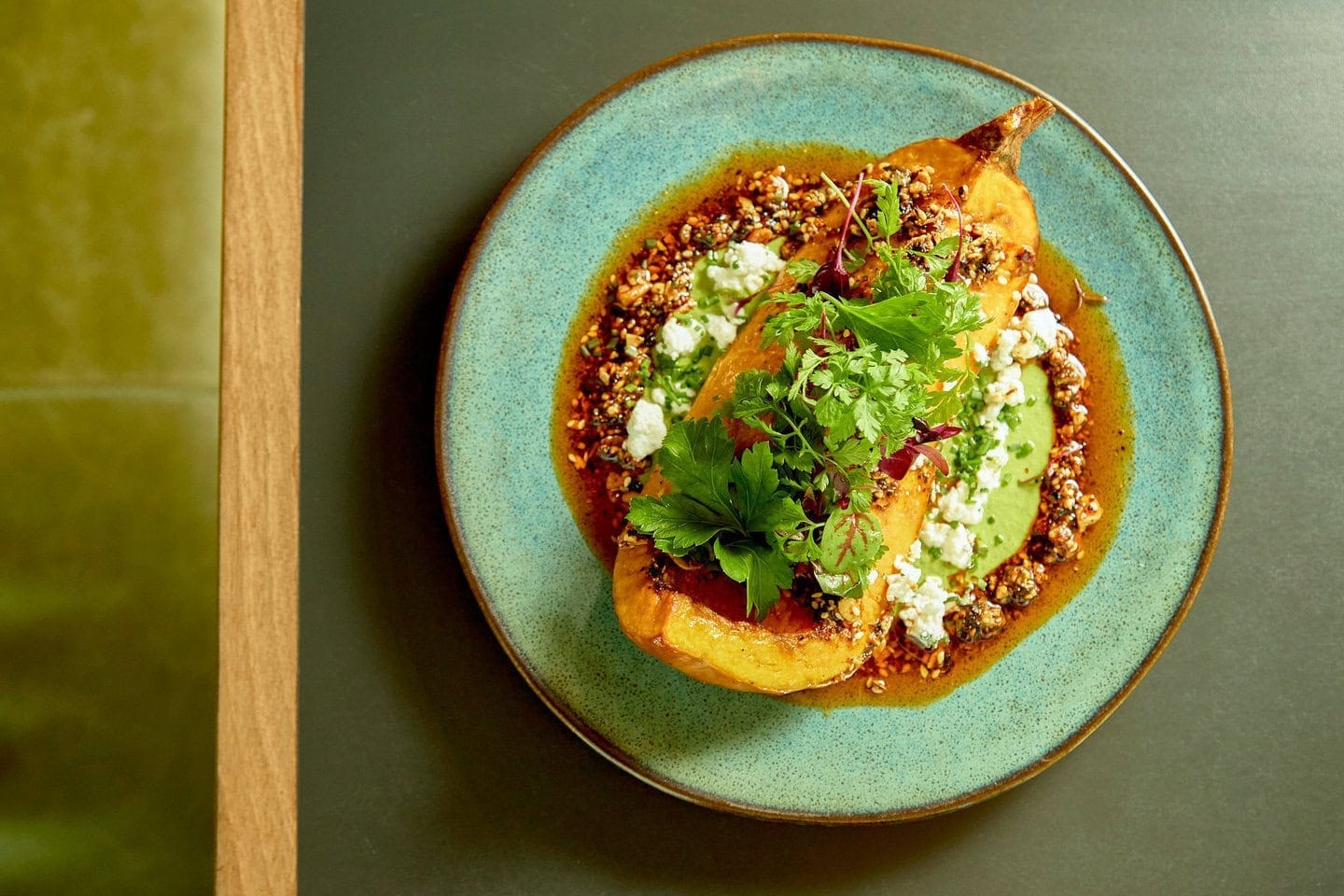 A segment of orange organic roasted squash sits on a bed of cashew nut & herb mole and salsa macha, topped with a microherb salad. This vegan dish is served across our Mexican restaurants in the UK.