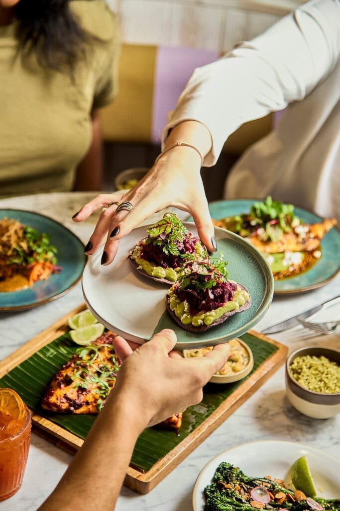 people share a plate of mexican style beetroot and avocado crema on a crisp tostada in a restaurant